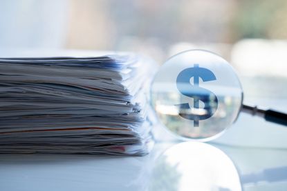 image of files on a table next to a magnifying glass over a dollar sign