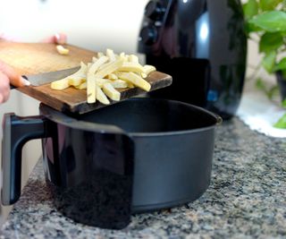 A black air fryer being filled with raw fries