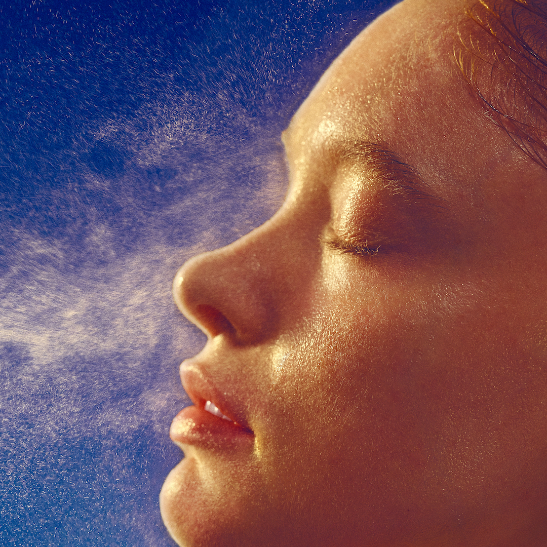 best face mists - image of a woman spraying a mist onto her face side on - gettyimages 1785634303