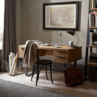 neutral home office with wooden desk, gray rug, gray curtains, and a map print on the beige wall