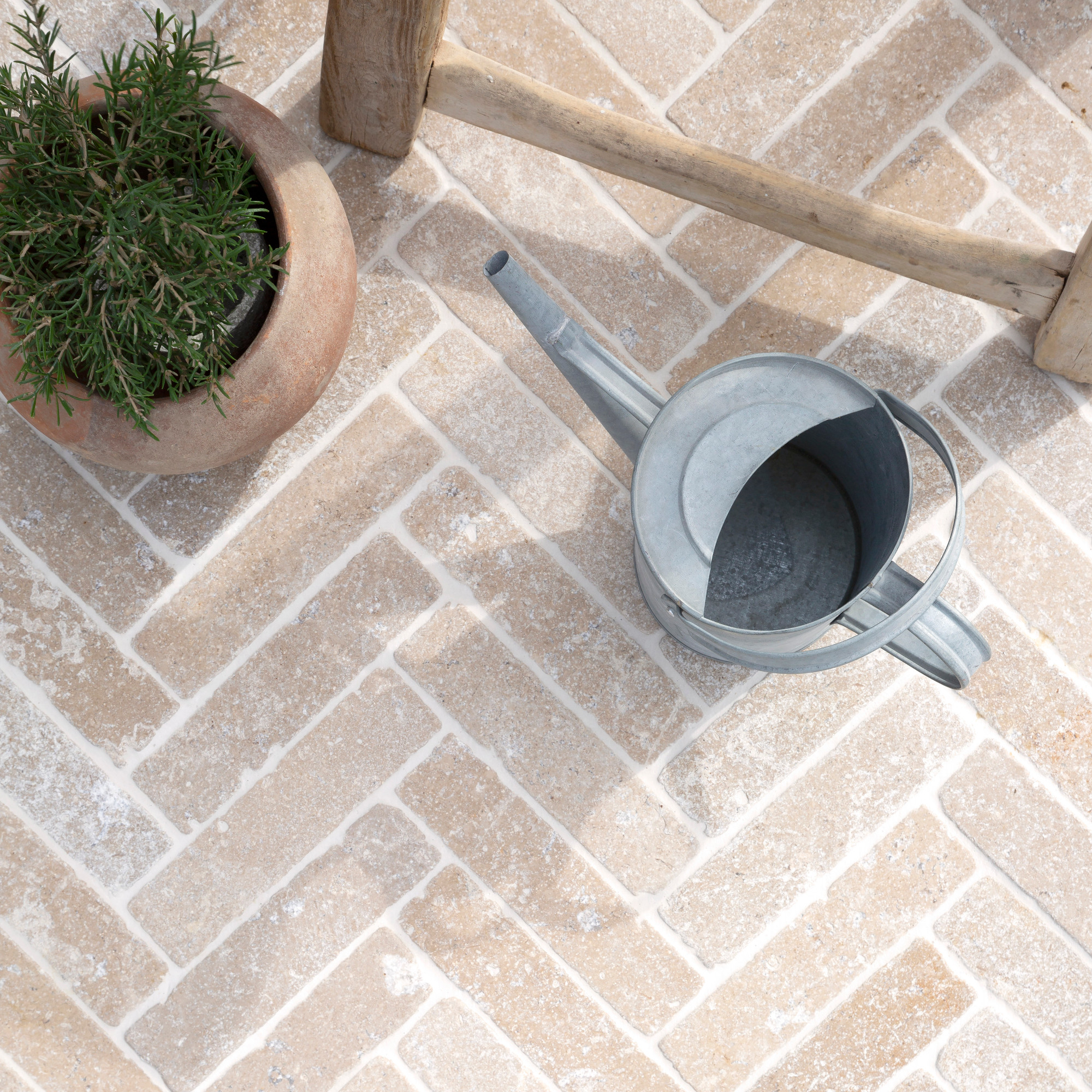 quorn stone dijon tumbled herringbone paving with watering can, plant pot and chair