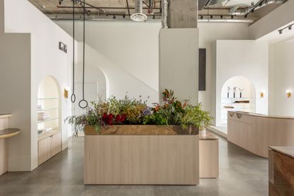 Cadine shop interior with concrete floor and white walls, furniture in granite and ash wood. A large wood and granite desk is visible in the middle of the room, with an installation of colourful wild flowers taking over its whole surface