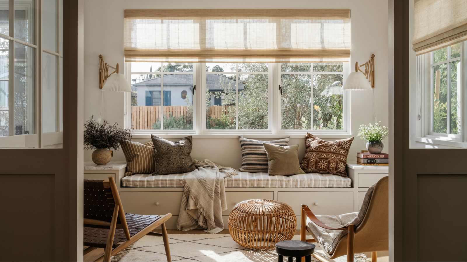 Coastal style lounge with built-in bench decorated with neutral cushions, a Berber rug, midcentury wooden lounge chairs and a rattan ottoman 