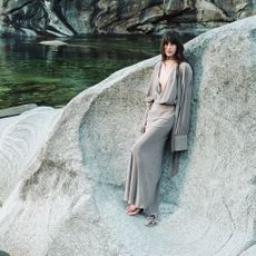 Young woman stood on rock near water wearing silver ThedoubleF dress