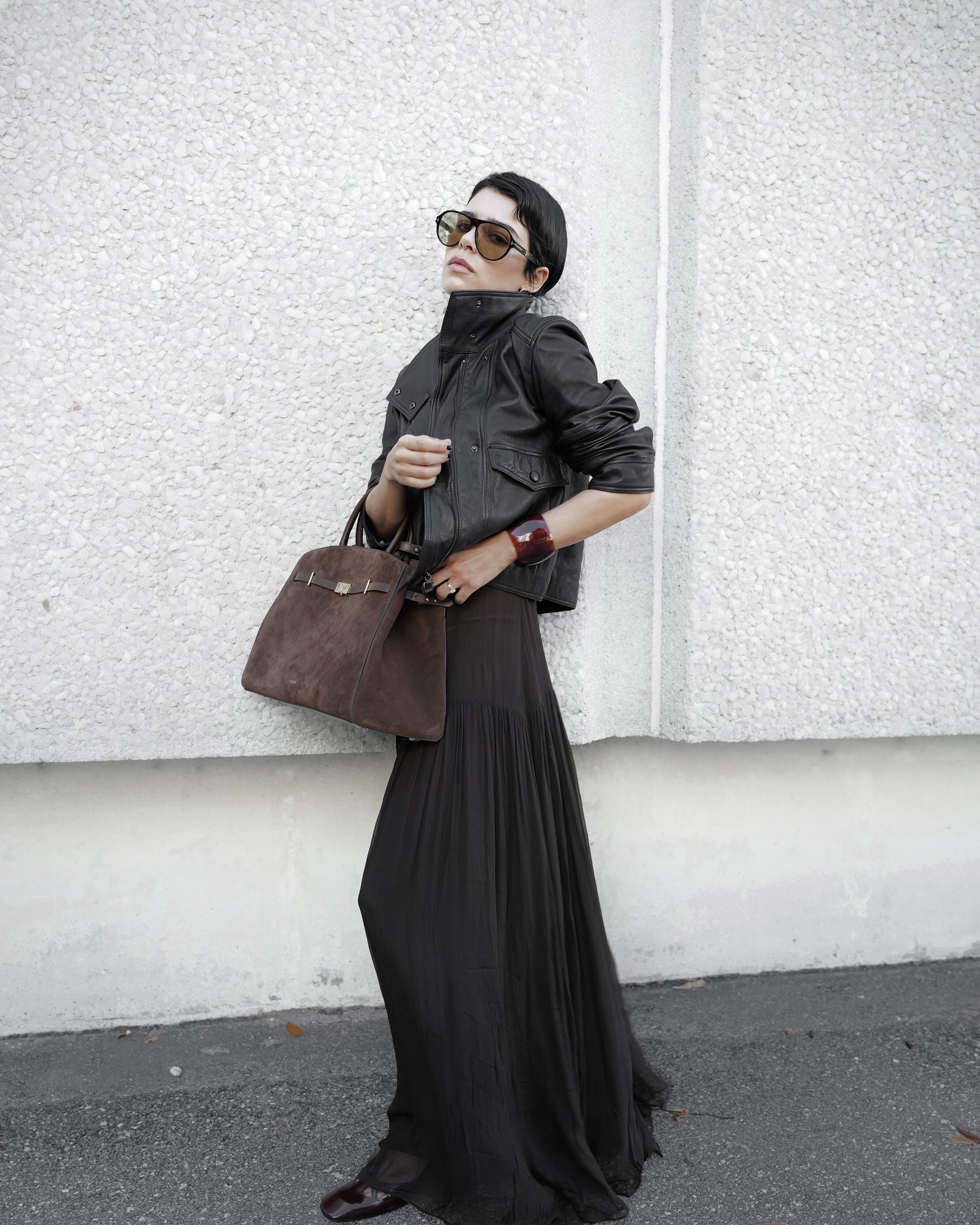 An image of @endlesslyloveclub wearing a leather funnel neck jacket with a pleated maxi skirt and suede Manu Atelier bag.