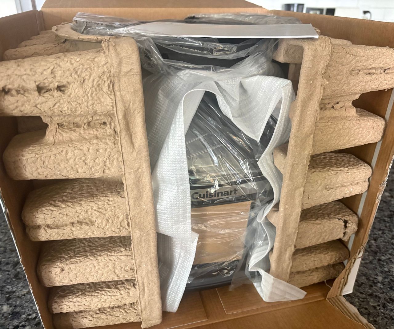 The Cuisinart glass air fryer inside cardboard packadging on a granite countertop