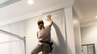 Person putting up patterned wallpaper in bedroom