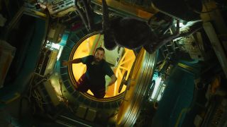 A bearded man floating inside a spaceship. He is shocked to discover a large spider-like creature floating opposite him.