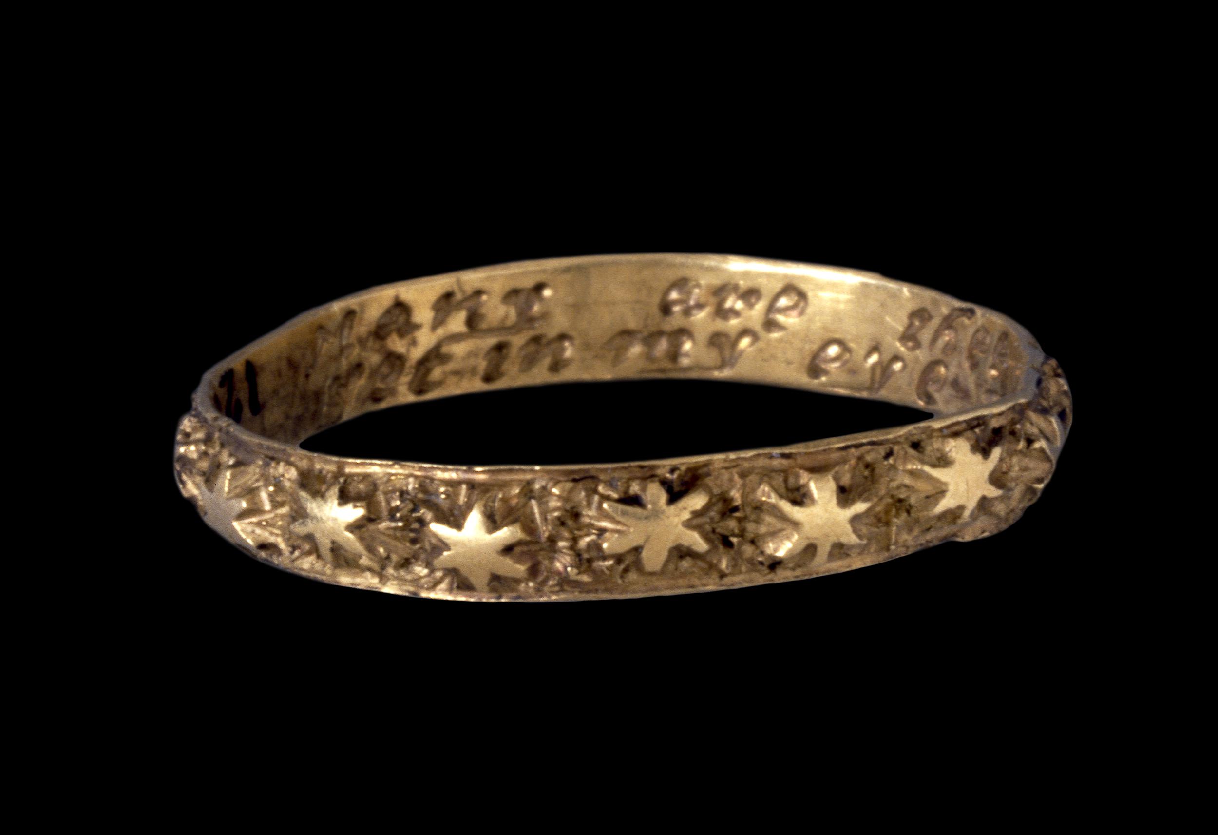 Gold posey ring engraved with stars on a black background