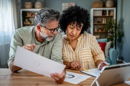 Worried mature couple feeling frustrated while trying to get their finances in order, looking at a tablet.