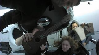 Chris Sembroski holds up the ukulele that he brought along on the Inspiration4 mission. In the background, Sian Proctor shows off her space art.