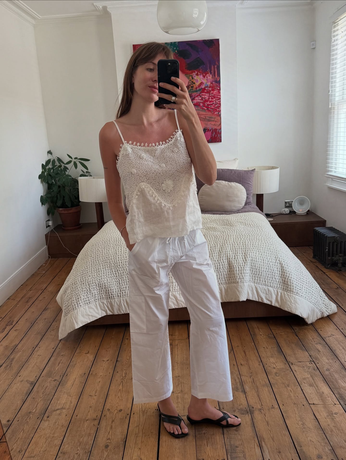 A woman wearing white tie-waist pants, lace top, and strappy black sandals.