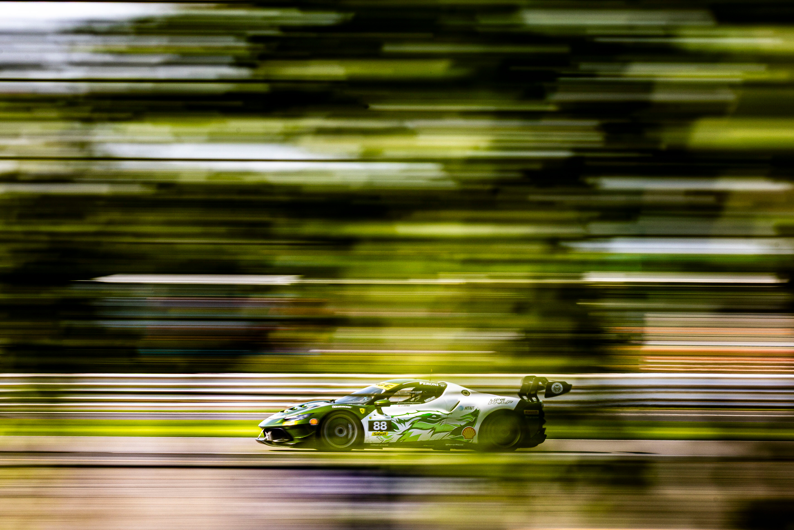 Racing car number 88 with green and white design speeds on track, motion blur in background and foreground