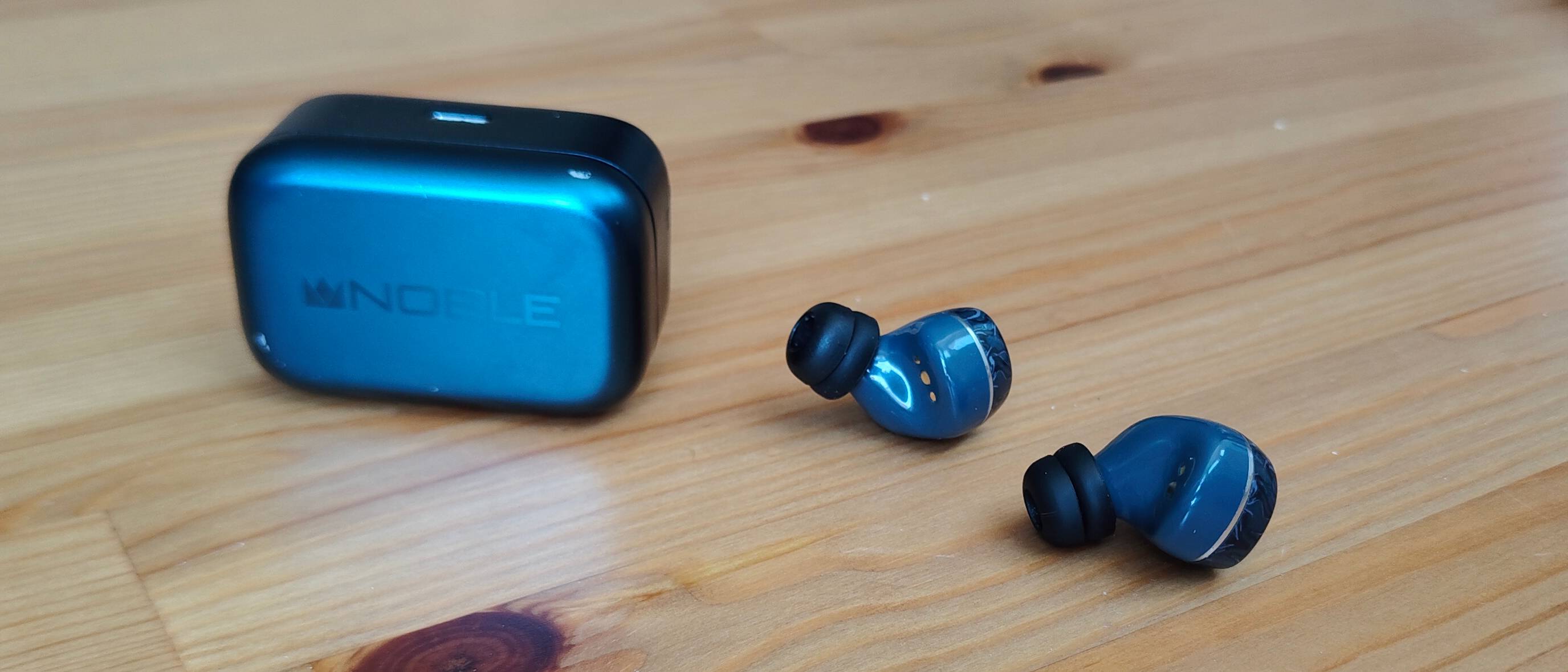 The Noble Osprey earbuds, on a table next to the case.