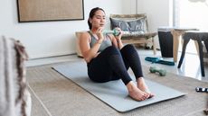 A woman does a crunch exercise at home with a light dumbbell