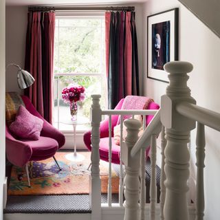 A landing sitting area with pink and black curtains, two pink armchairs, and an orange rug