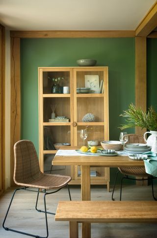 rustic dining room with green walls, rattan chairs, matching wooden table, benches and cabinet