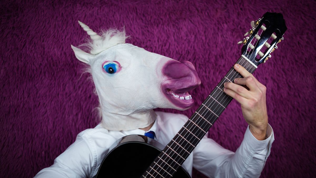 Freaky young man in comical mask playing the guitar on the purple background.