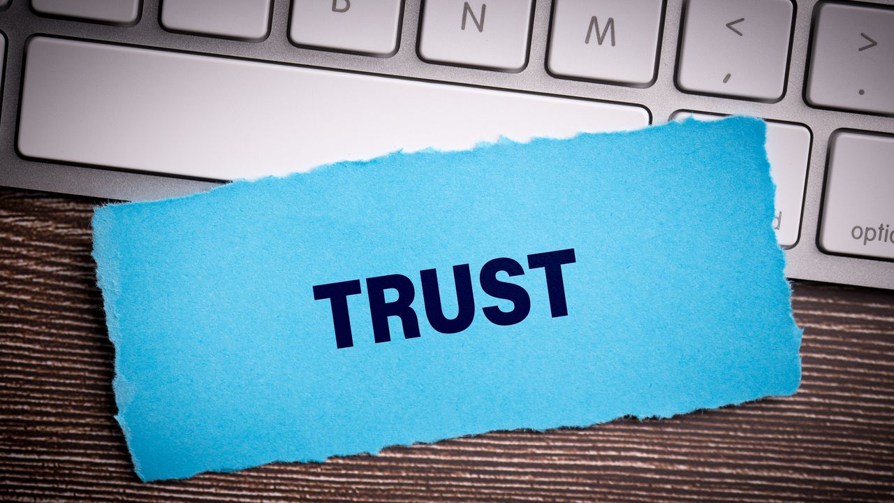 The word &quot;trust&quot; on blue paper sitting on a laptop keyboard.