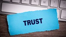 The word "trust" on blue paper sitting on a laptop keyboard.