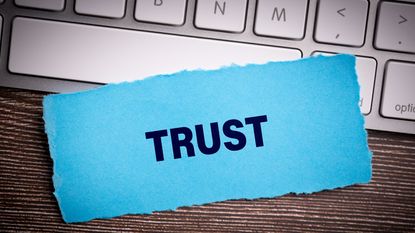 The word &quot;trust&quot; on blue paper sitting on a laptop keyboard.