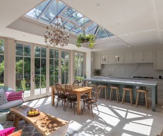 orangery kitchen extension with large rooflight, metal and glass chandelier and plants hanging from rooflight and kitchen, dining and seating area below