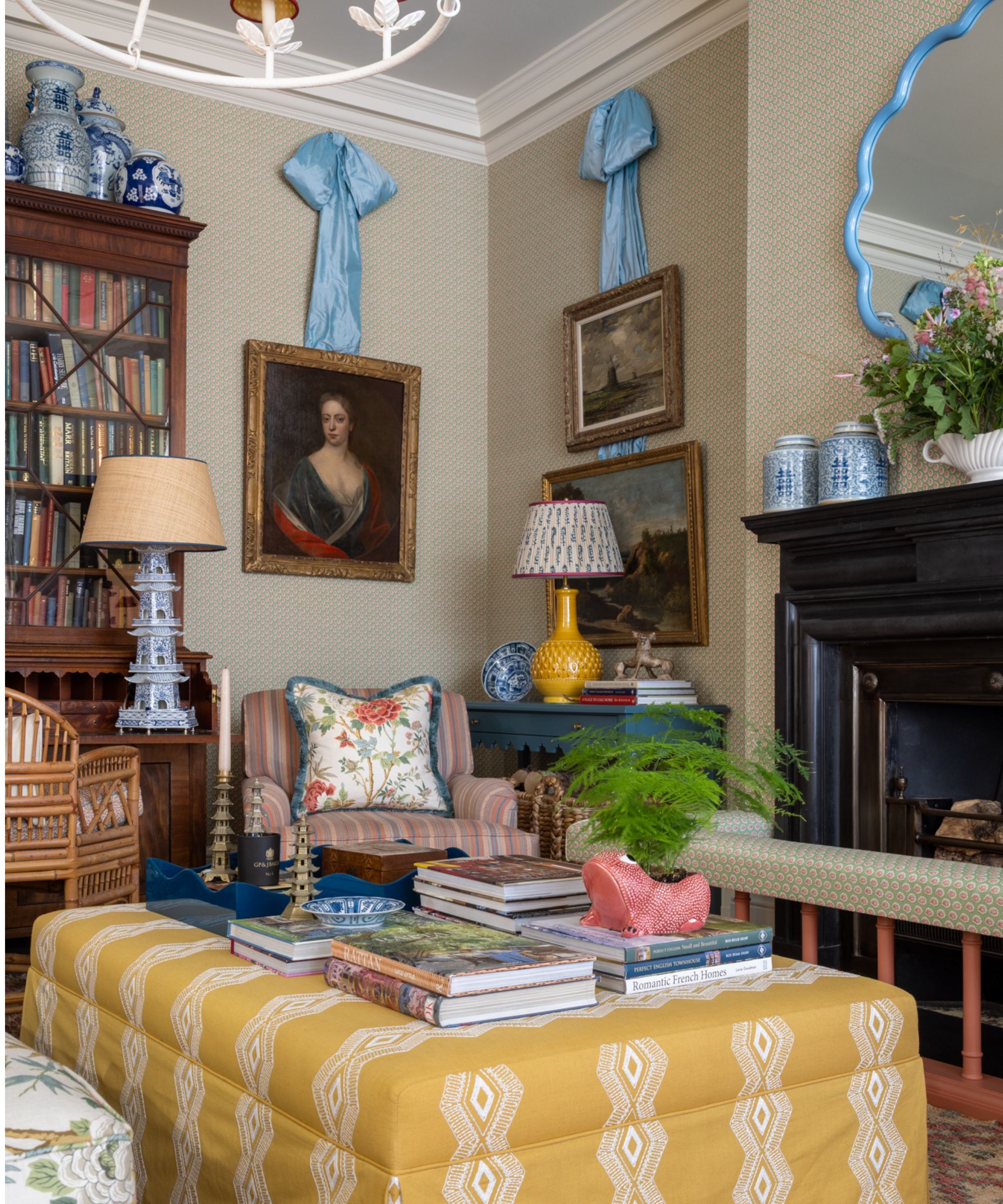 vintage traditional english country living room with a black fireplace, an antique bookcase, vintage art, a yellow upholstered ottoman