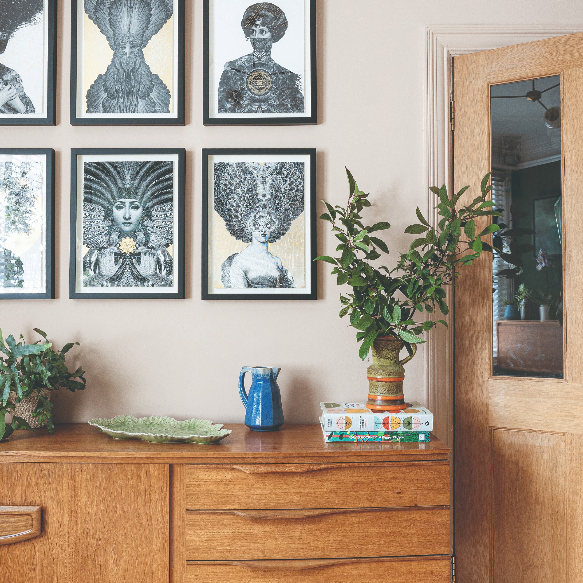 A soft pink-painted living room with a midcentury modern sideboard displaying a vase of foraged branches