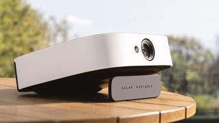 The Anker Nebula Solar Portable projector on a wooden table outside with trees in the background