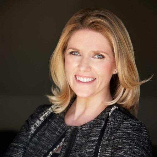 Image of a woman in a charcoal blazer standing in front of a dark background.