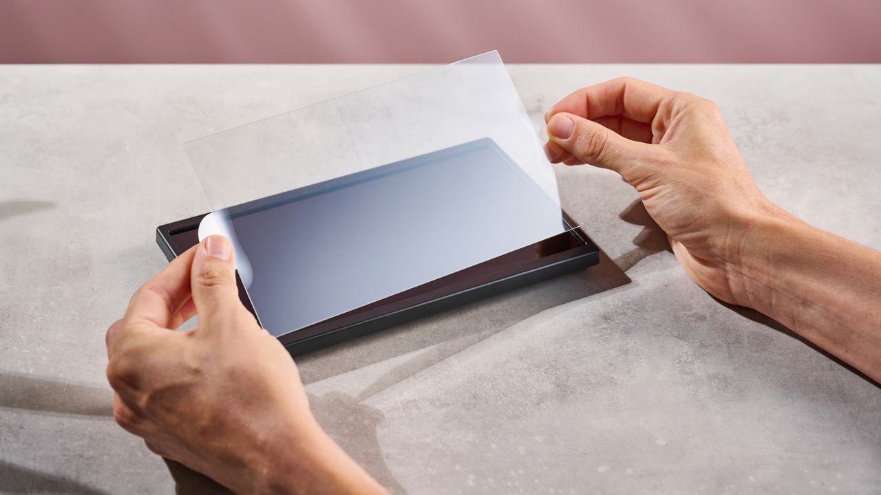 A man lifting and preparing to apply the Belkin Tempered Glass Anti-Reflective Screen Protector to the Nintendo Switch 2.