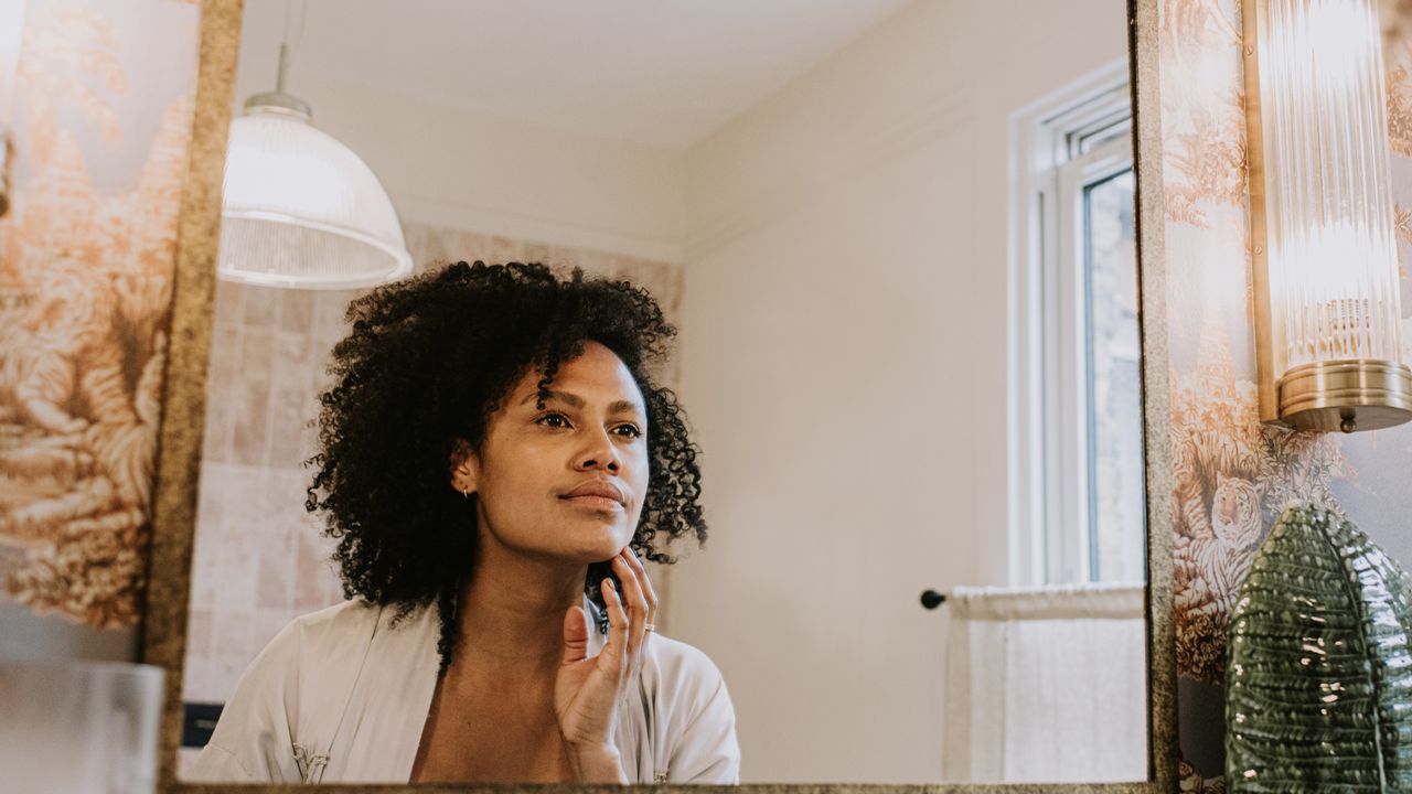 woman looks in the mirror to check for acne