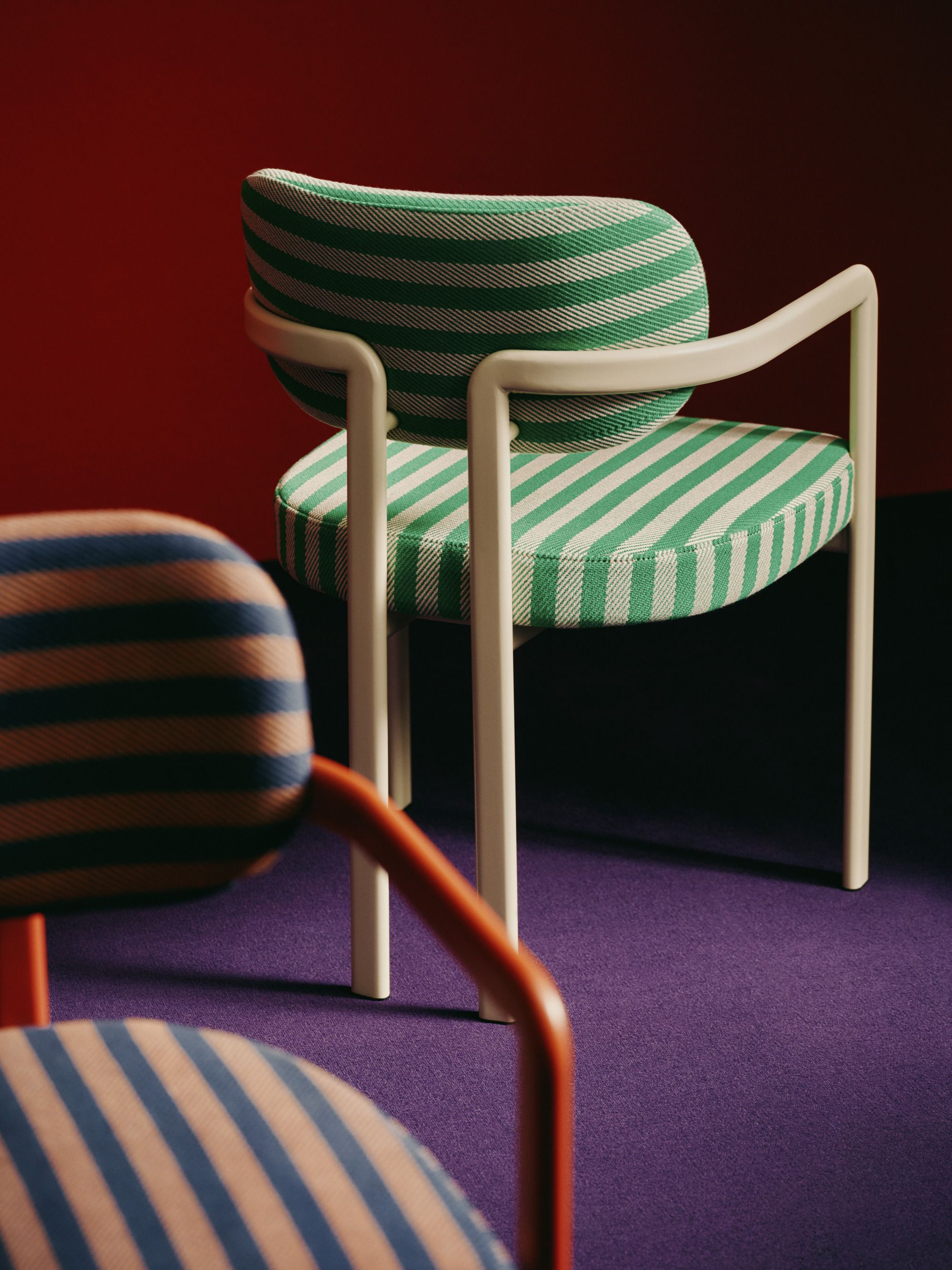 Image of a green and white chair and an orange and blue chair positioned back to back on a purple carpet in a room with red walls.