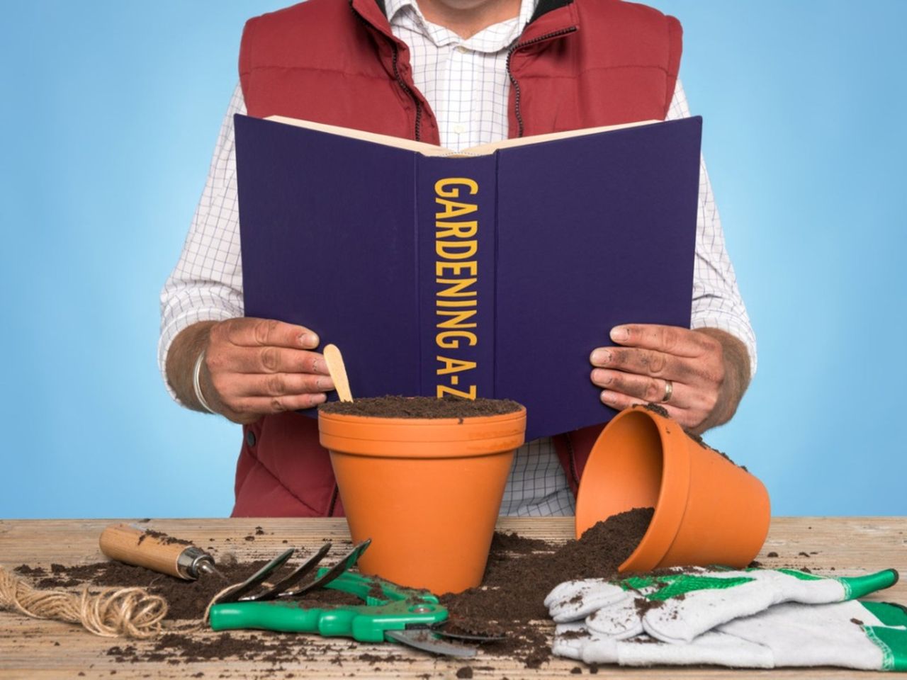 Person Reading A Gardening Book With Pots Soil And Gardening Tools