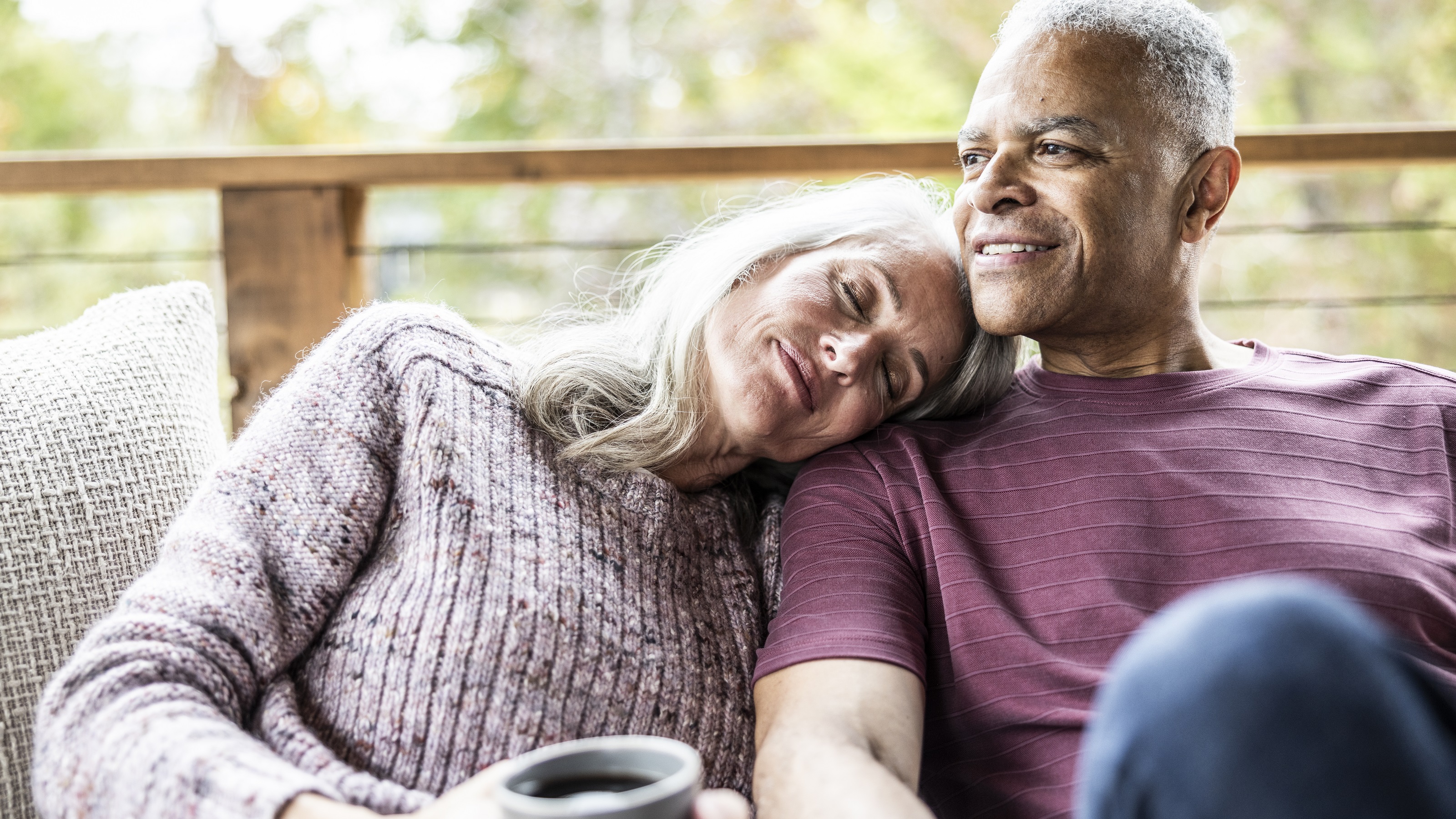 A retired couple relax on their deck, looking happy.
