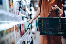 A person carrying a black, plastic supermarket basket while shopping for supermarket groceries.