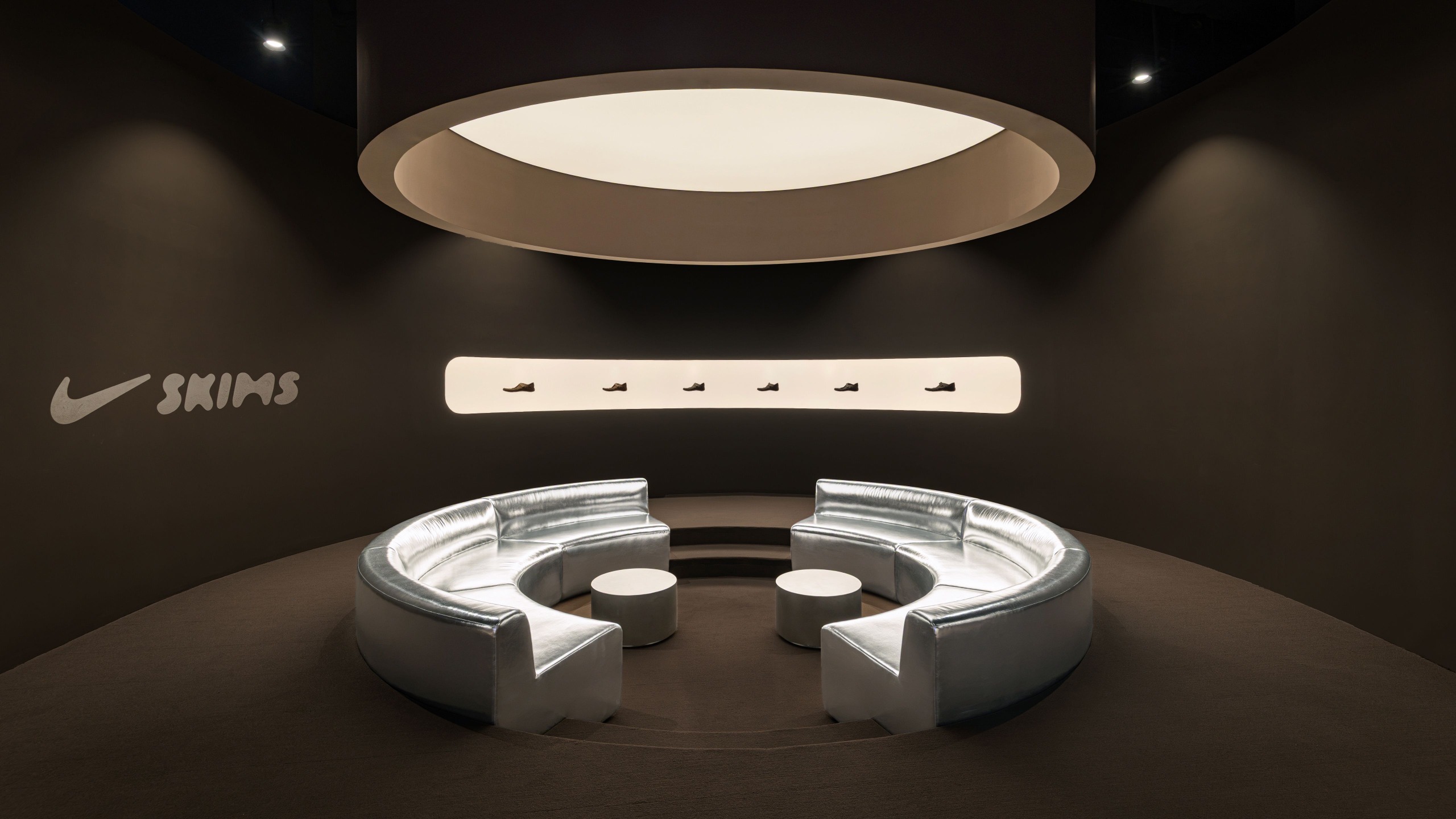 An activewear store decorated with opaque brown walls mixed with glossy chrome detailing and back-lit surfaces.
