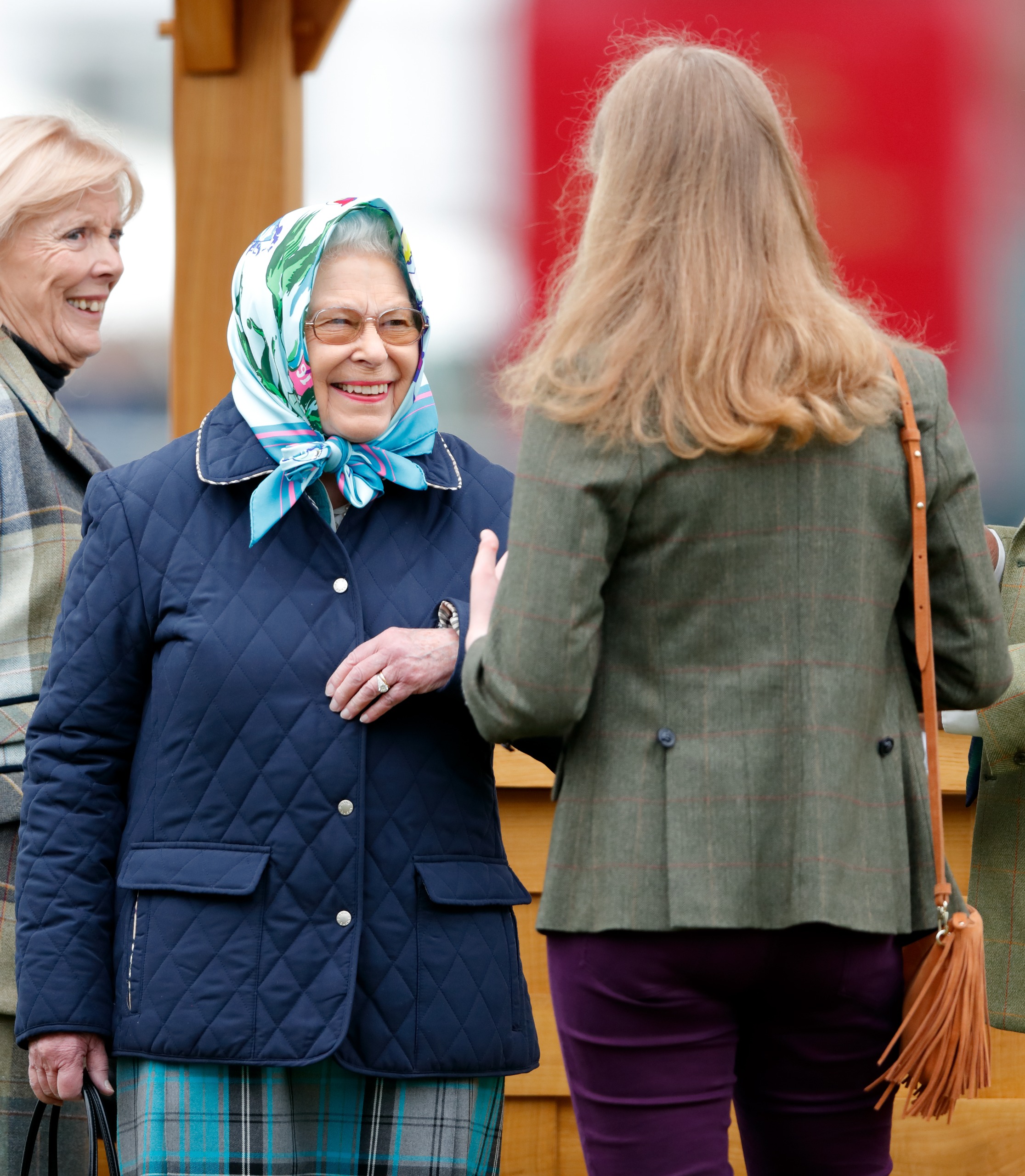 Queen Elizabeth wearing a blue quilted coat and a head scarf smiling at Lady Louise