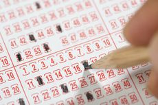 Close-up of a male hand filling lottery ticket with pencil.