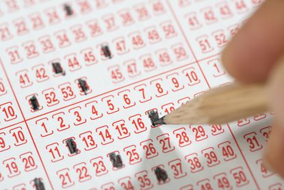 Close-up of a male hand filling lottery ticket with pencil.