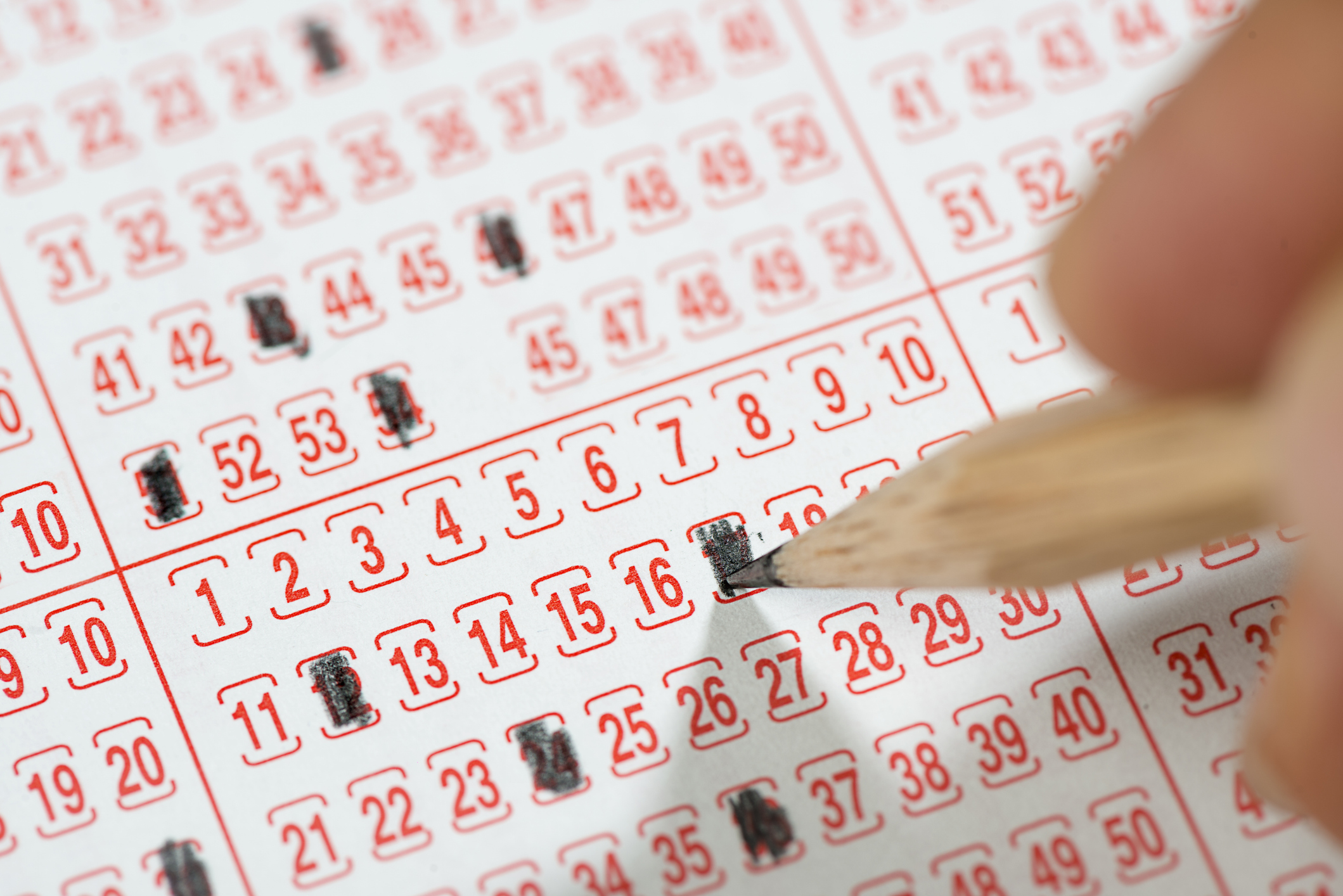 Close-up of a male hand filling lottery ticket with pencil.