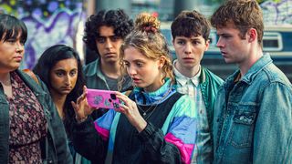The cast of the BBC and Netflix's Red Rose, huddled around Amelia Clarkson as Wren Davies who is looking into a phone.