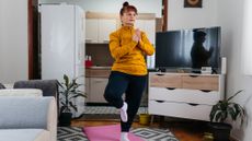 Woman standing on one leg in yoga pose in living room