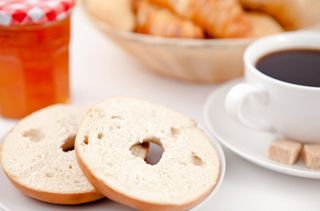 Doughnut cut in half and a cup of coffee on white plates with sugar and milk and a pot of jam