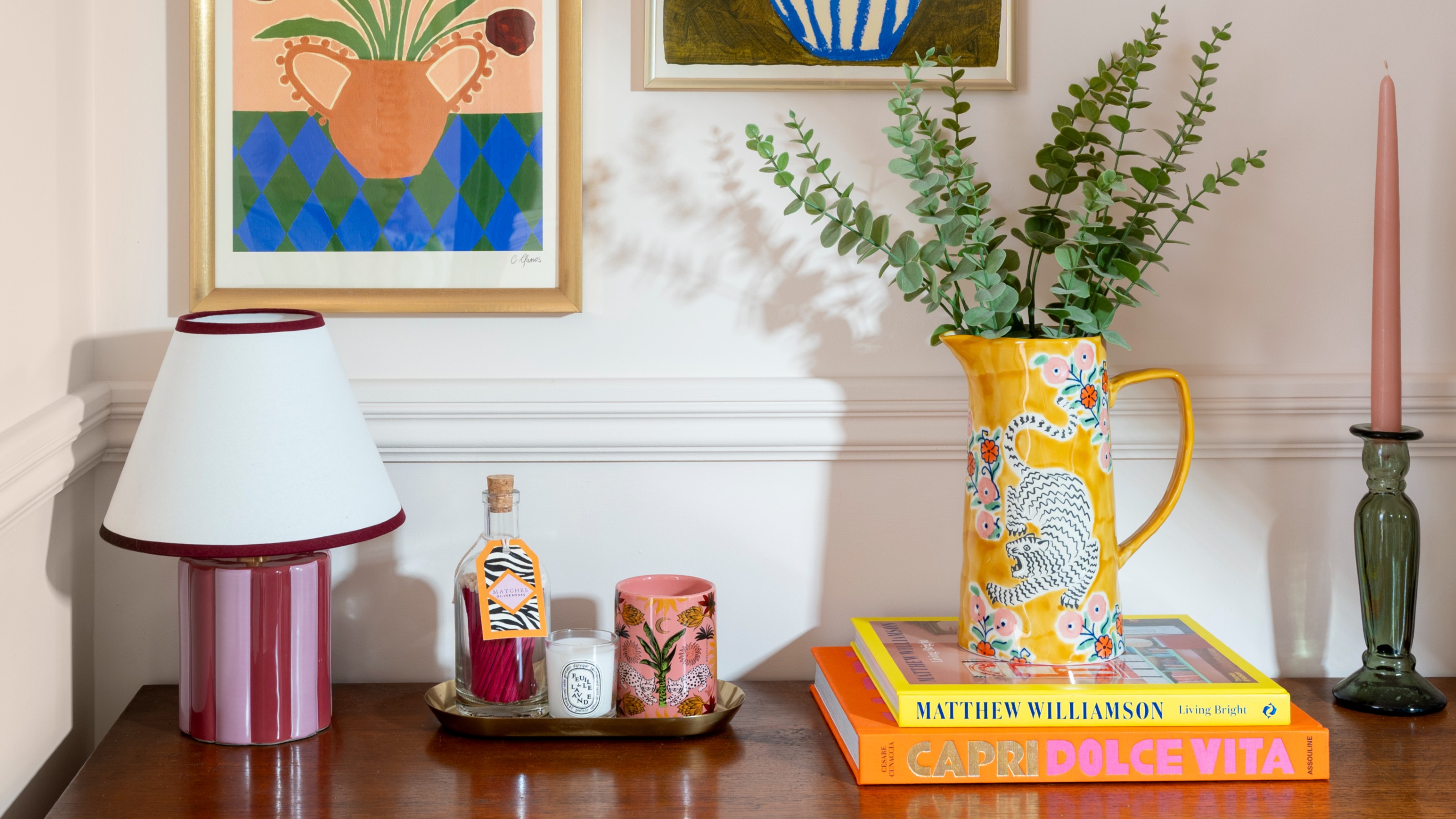 A sideboard styled with a striped table lamp, coffee table books and tiger-motif jug with eucalyptus branches