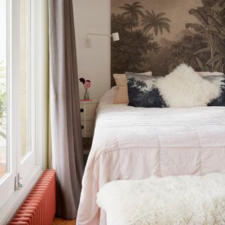 bedroom with a bed beside a window and a coral painted radiator and a tropical artwork behind the bed head