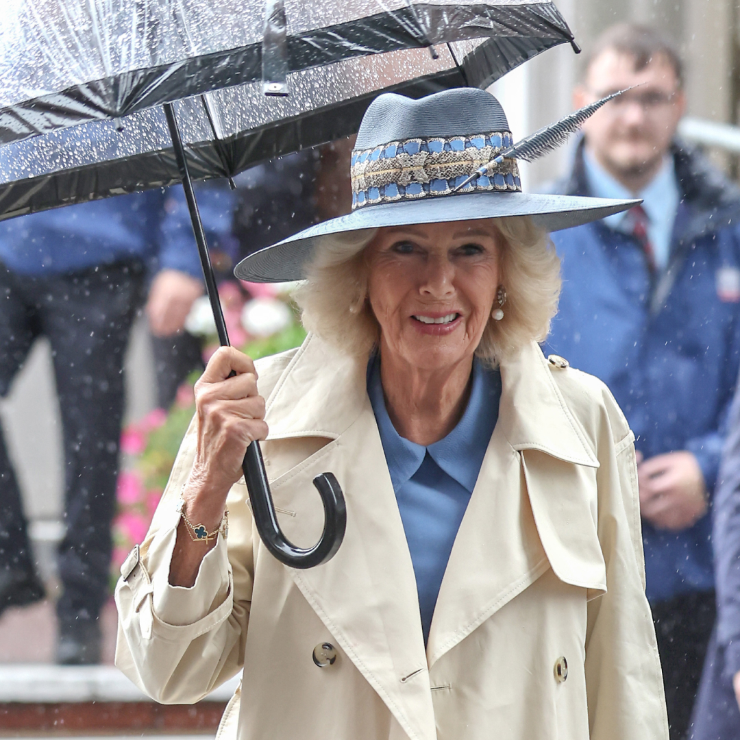 Queen Camilla holding an umbrella wearing a trench coat and hat