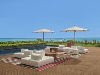 white outdoor furniture, sun umbrellas and a pool with ocean beyond