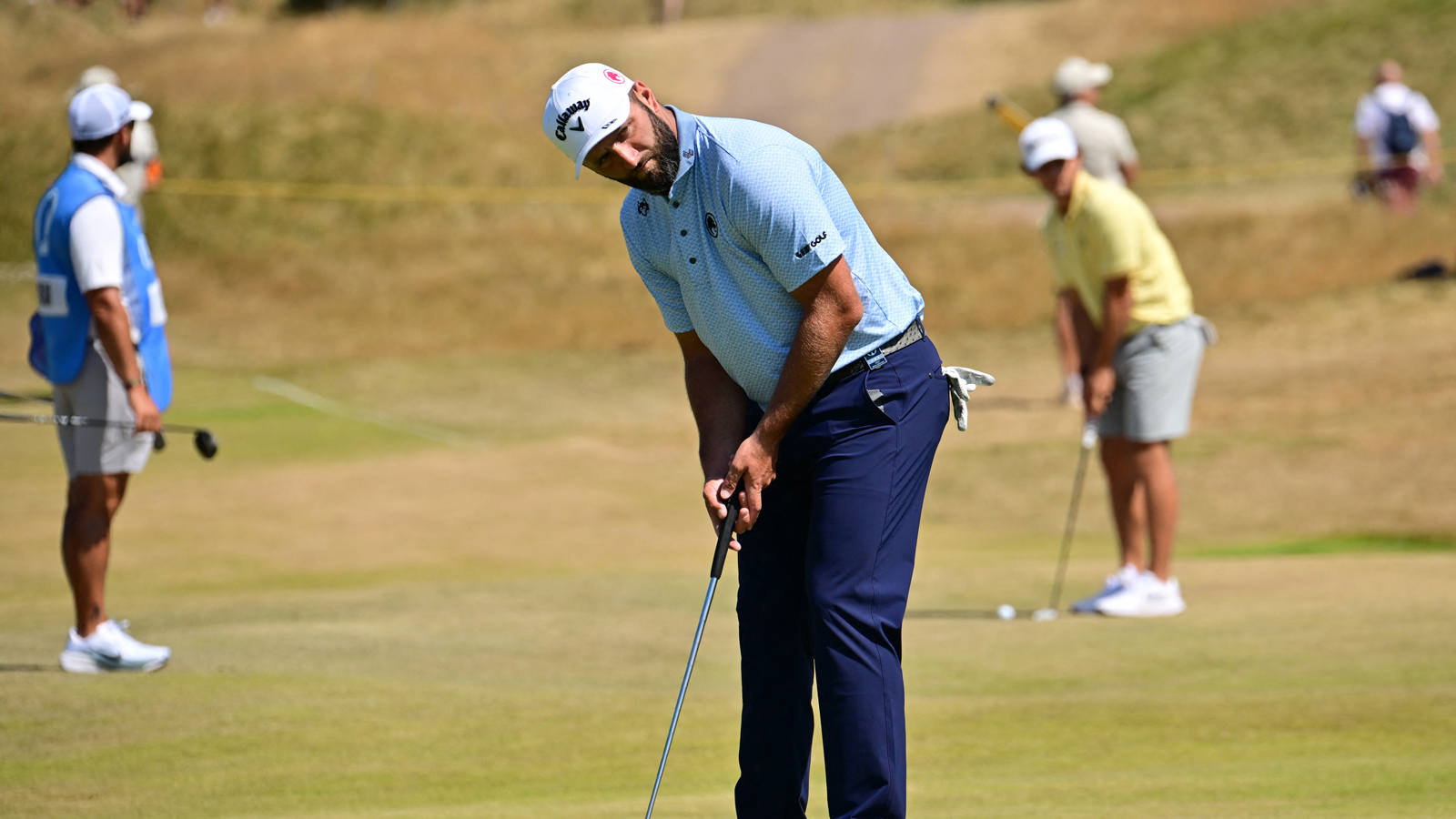 Jon Rahm hits a putt with another golfer behind him