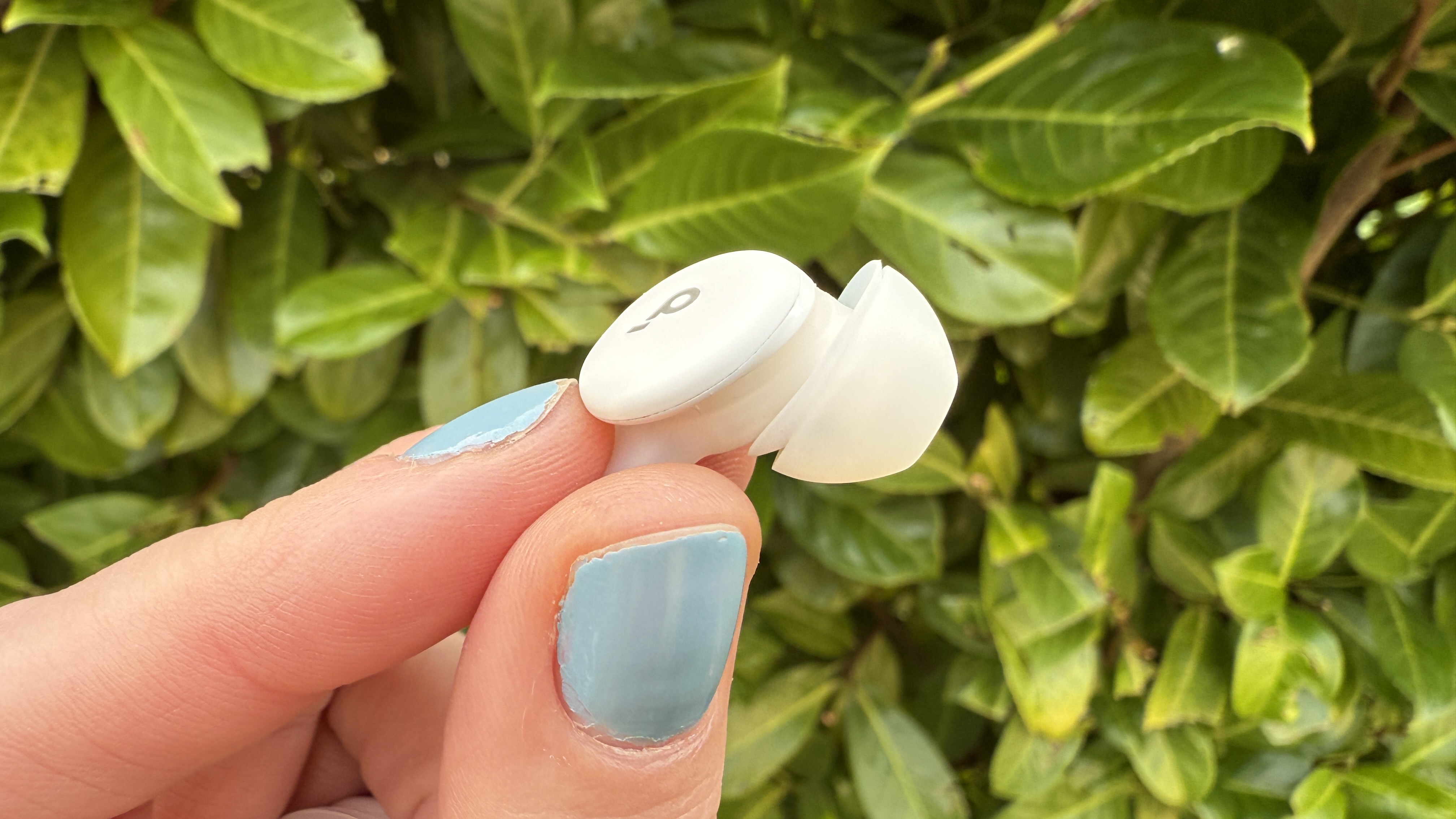 Someone holding one of the soundcore sleep a30 earbuds against a green hedge.